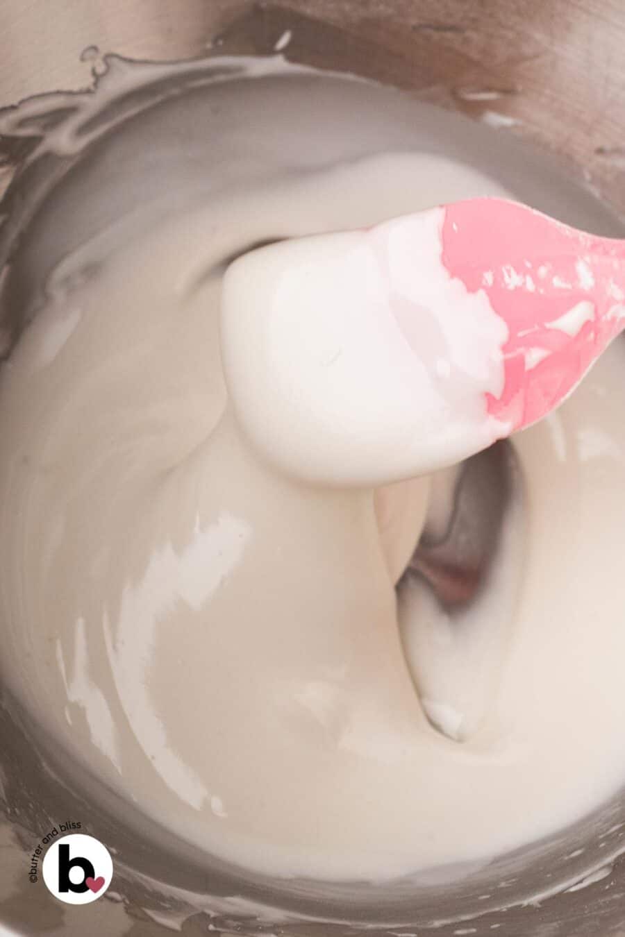 Glossy royal icing in a mixing bowl with a pink spatula.