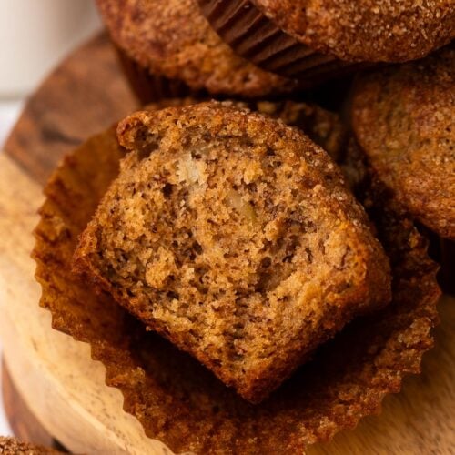 A banana muffin on a wood plate, cut in half to reveal a moist crumb studded with walnuts.