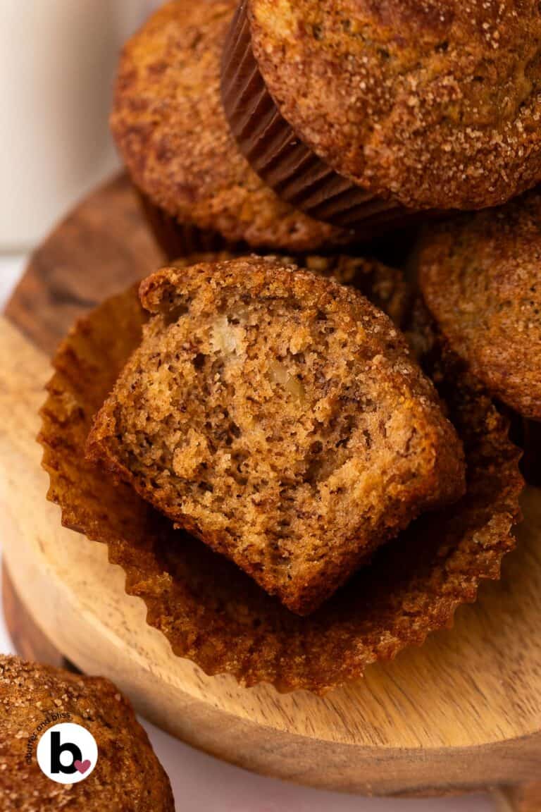 A banana muffin on a wood plate, cut in half to reveal a moist crumb studded with walnuts.