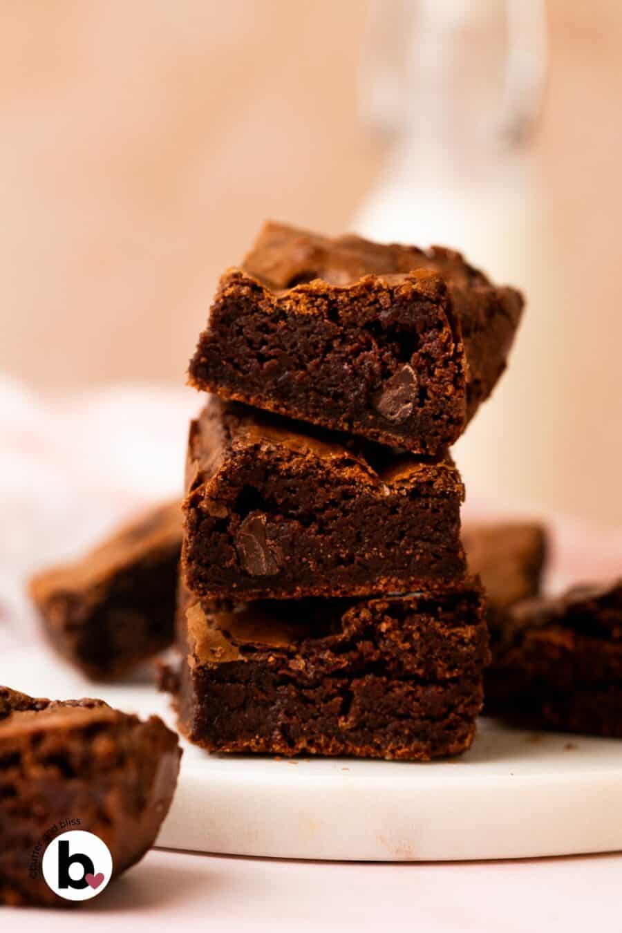 A stack of three fudgy brownies on a white plate next to a glass of milk.
