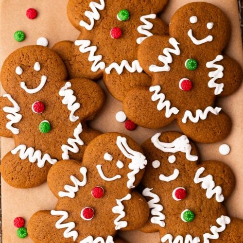Gingerbread man cookies decorated with royal icing for Christmas on a piece of parchment paper.