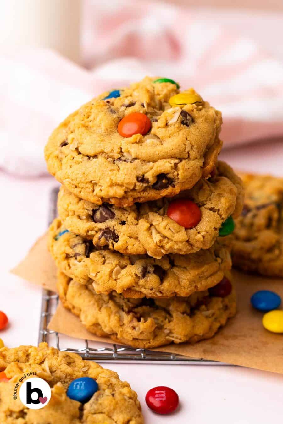 A small stack of monster cookies studded with M&M's on a wire rack next to a glass of milk.