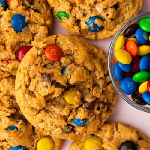 Small batch of monster cookies piled on a table next to a bowl of M&M's.
