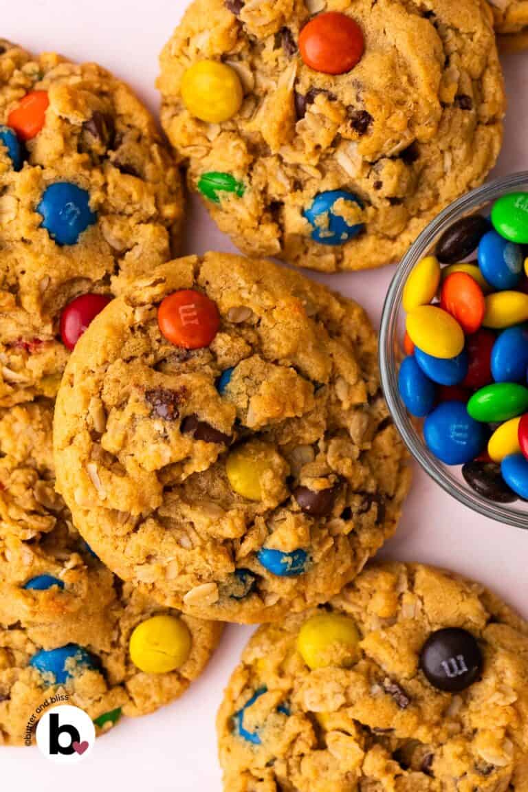 Small batch of monster cookies piled on a table next to a bowl of M&M's.