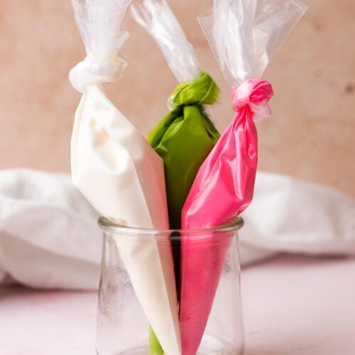 Three different colors of royal icing in piping bags, set in a small jar.