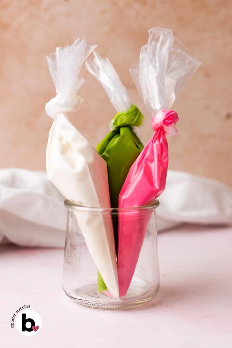 Three different colors of royal icing in piping bags, set in a small jar.