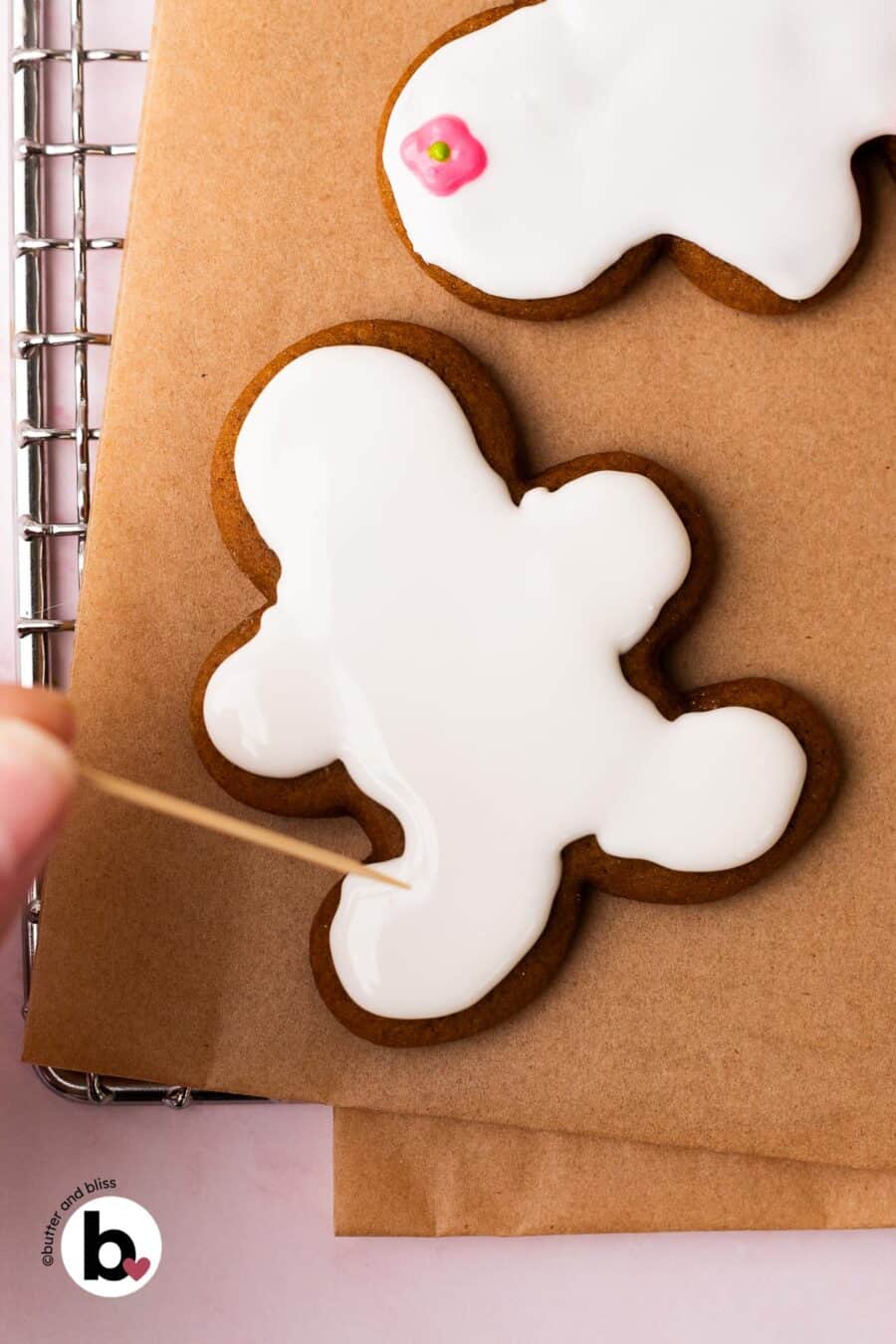 Hand spreading royal icing onto a cookie with a toothpick.