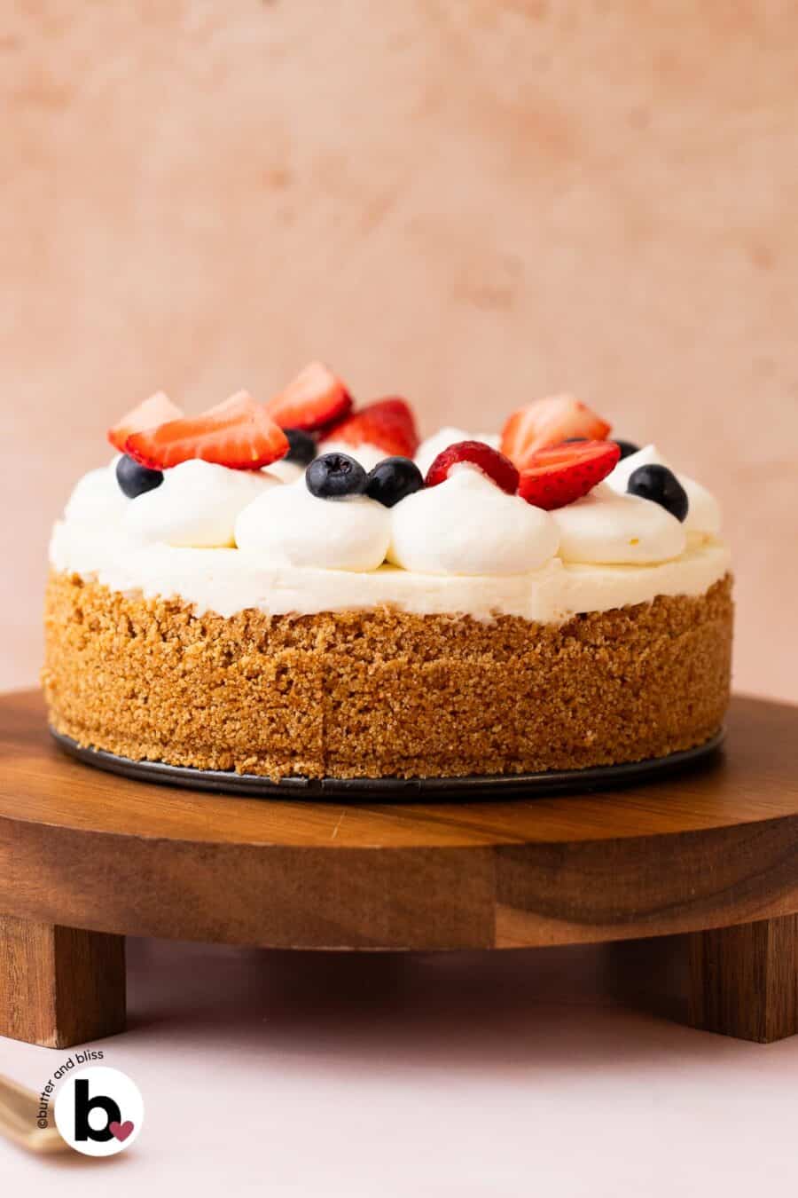 Small 6-inch no-bake cheesecake topped with whipped cream and fresh fruit on a wood cake stand.