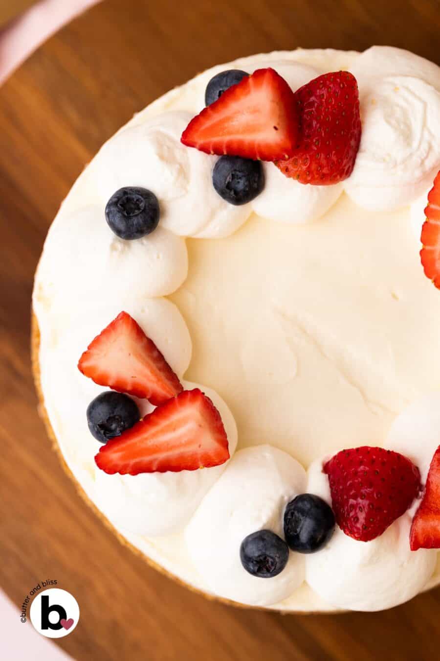 Top of a no-bake cheesecake topped with whipped cream and fresh fruit on a wood cake plate.