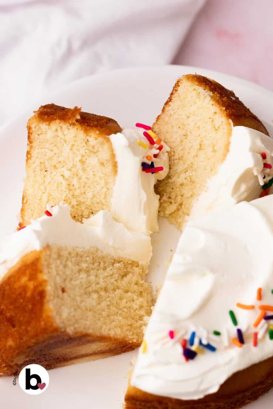 Small white cake with white frosting and colorful sprinkles cut into slices and arranged on a white cake platter.