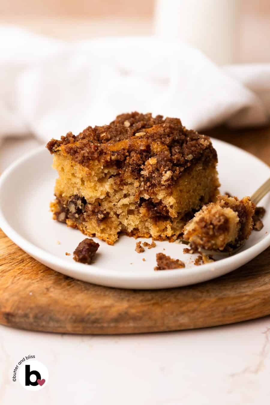 A slice of applesauce coffee cake on a white plate, with a fork piece cut into it .