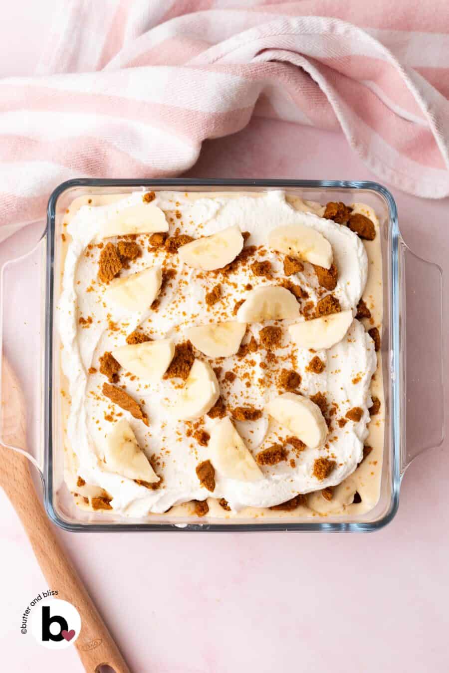 Small casserole dish with Biscoff banana pudding topped with whipped cream, banana slices, and crushed cookies.
