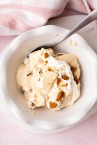Ruffled white bowl full of creamy Biscoff banana pudding with a spoon.