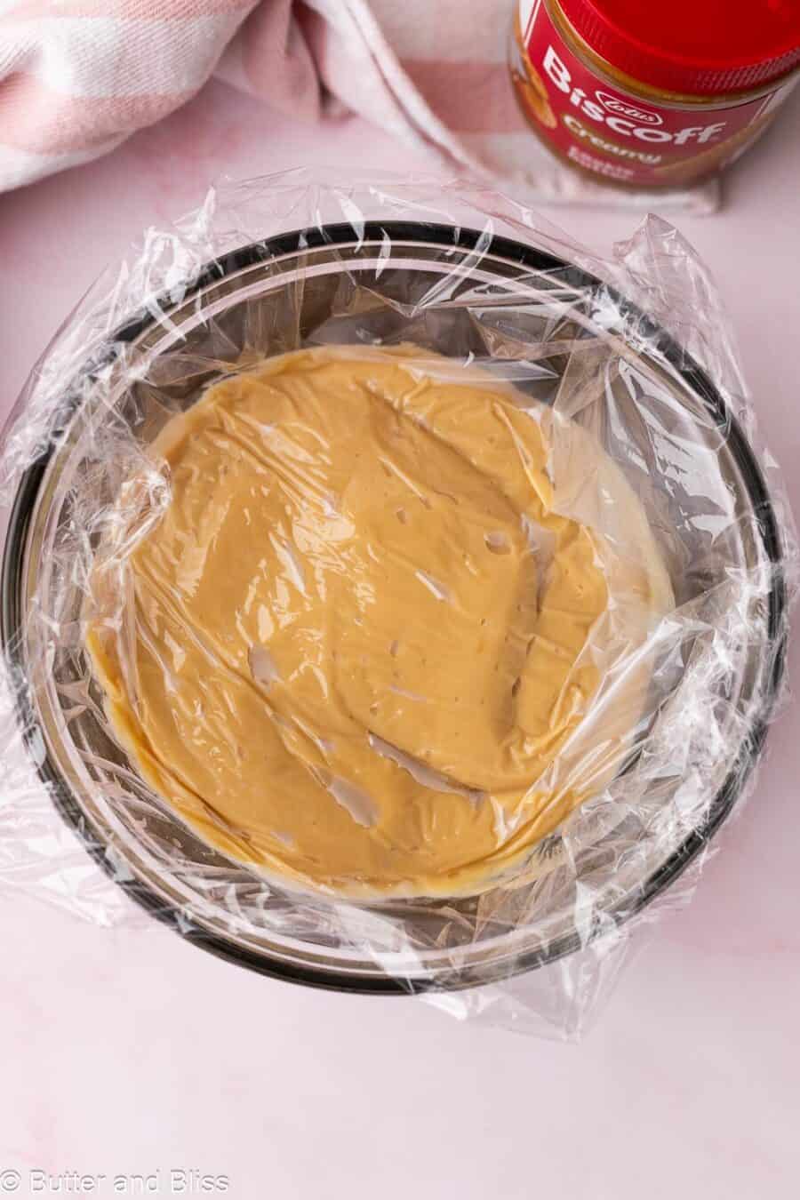 A bowl of cookie butter pudding covered with plastic wrap.