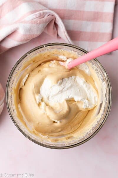 Whipped cream folded into creamy Biscoff banana pudding in a mixing bowl.