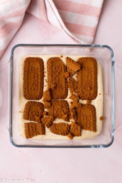 Biscoff pudding being layered with Biscoff cookies in a small casserole dish.