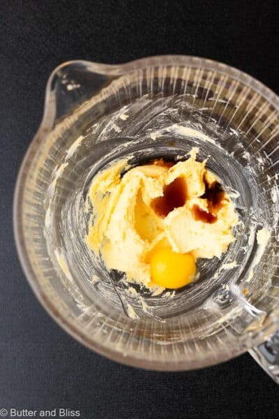 Egg yolk and vanilla added to creamed butter and sugar in a glass mixing bowl.