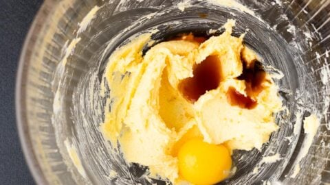 Egg yolk and vanilla added to creamed butter and sugar in a glass mixing bowl.