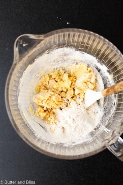 Flour added to wet cookie ingredients in a glass mixing bowl.