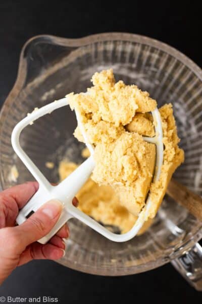 Hand holding thick butter cookie dough on a mixing paddle attachment.