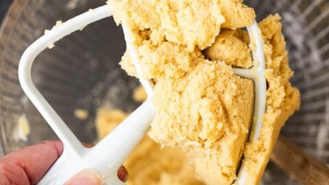 Hand holding thick butter cookie dough on a mixing paddle attachment.
