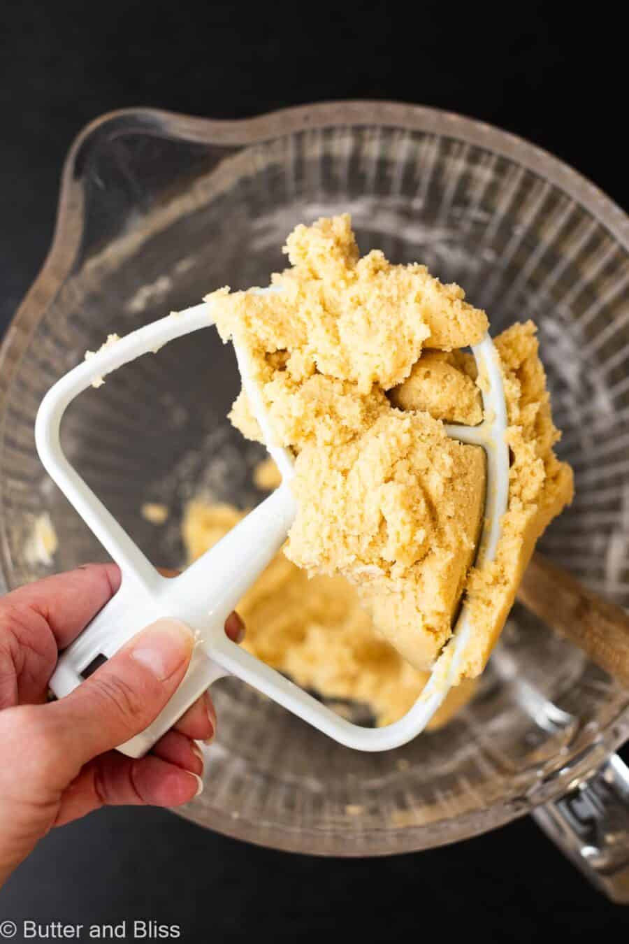 Hand holding thick butter cookie dough on a mixing paddle attachment.