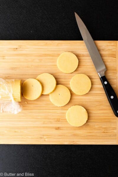 Butter cookie dough cut into discs on a wood cutting board.