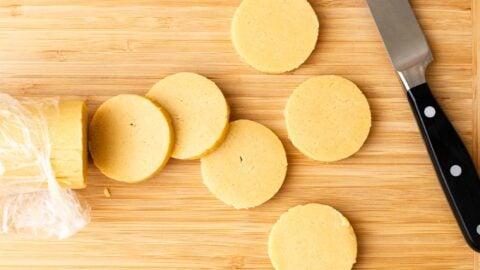 Butter cookie dough cut into discs on a wood cutting board.