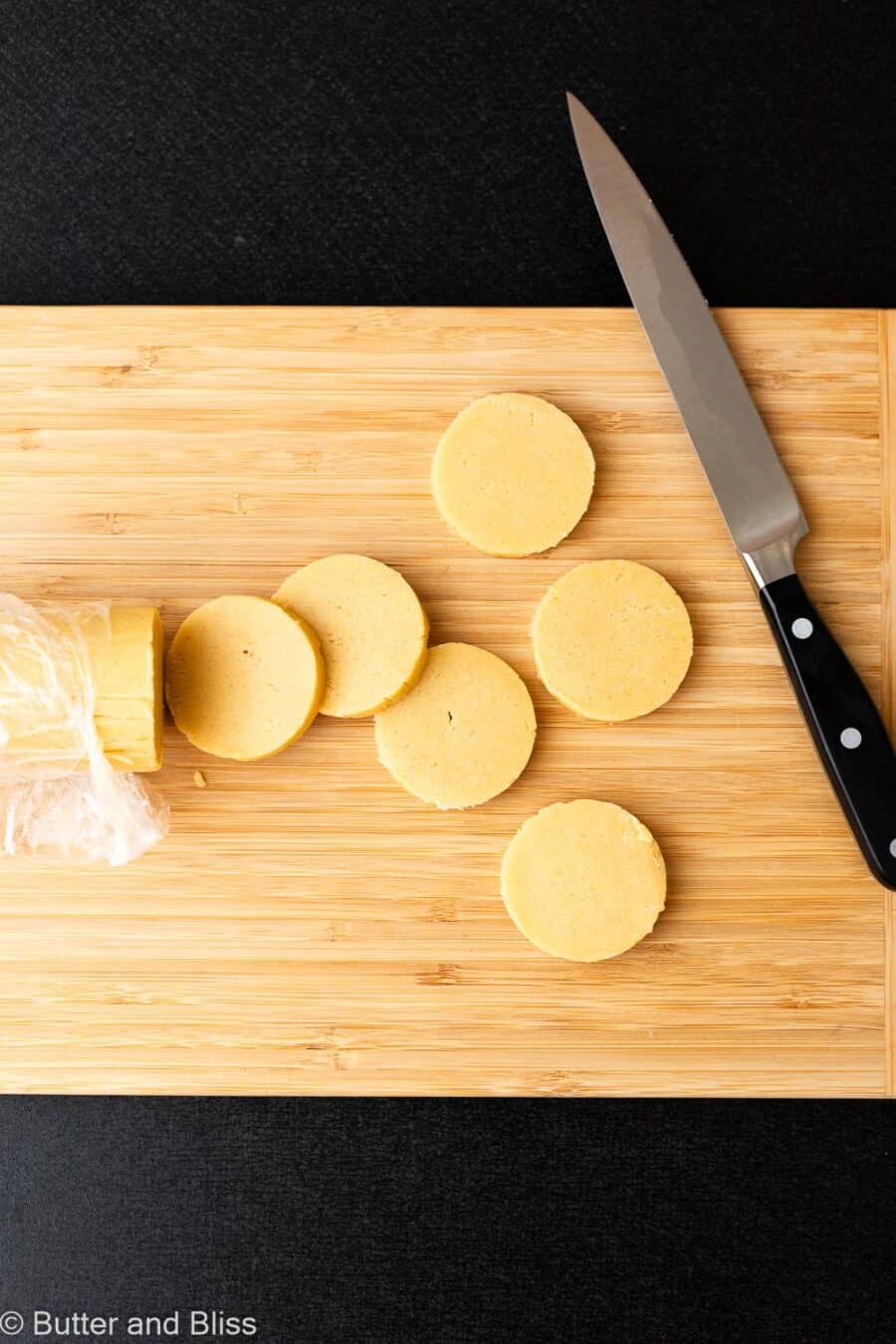 Butter cookie dough cut into discs on a wood cutting board.