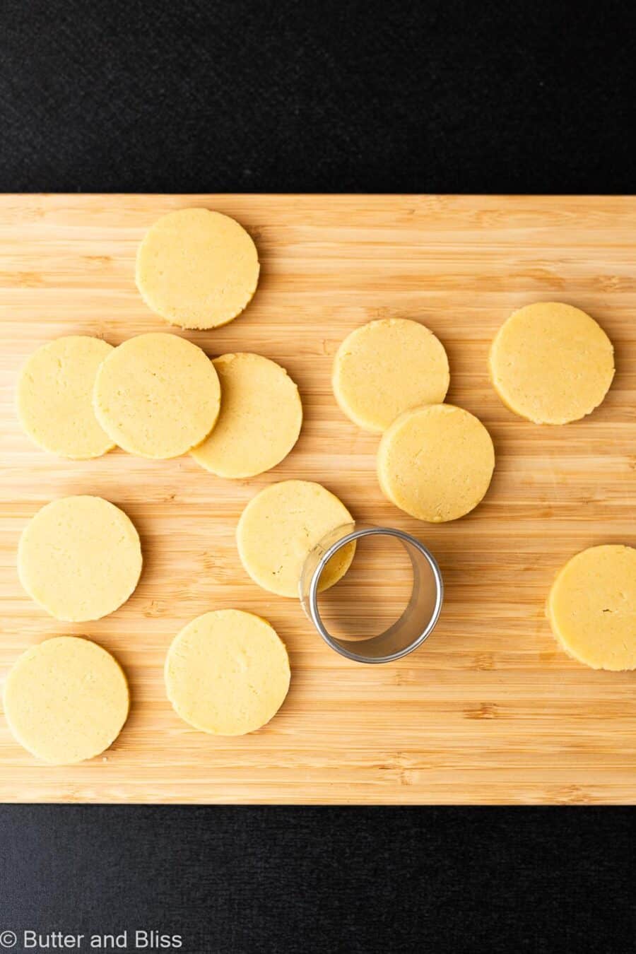 Small round cookie cutter cutting round butter cookie discs on a wood cutting board.