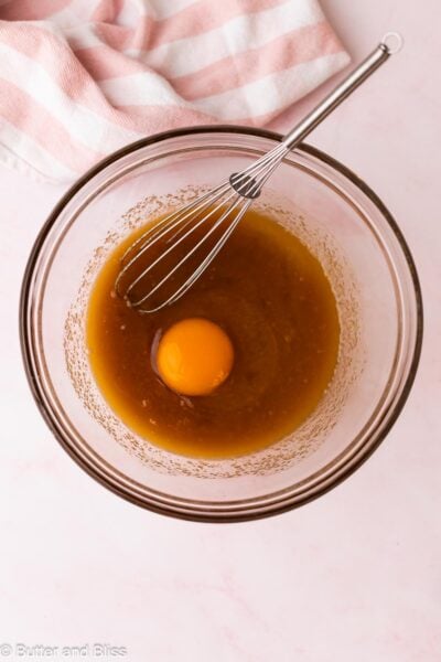 An egg added to melted butter and sugar mixture in a mixing bowl.
