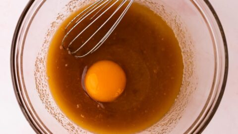 An egg added to melted butter and sugar mixture in a mixing bowl.