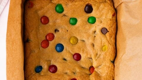 Fresh baked M&M cookie bars cooling in a square pan.