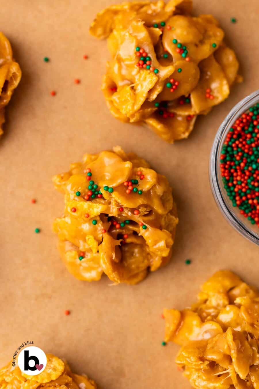 Peanut butter cornflake cookies decorated with red and green holiday sprinkles on a baking sheet.