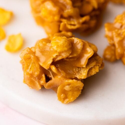 Shiny peanut butter cornflake no-bake cooie on a white marble plate.