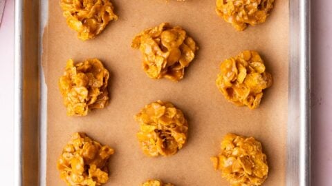 One dozen cornflake and peanut butter no-bake cookies set on a baking sheet.