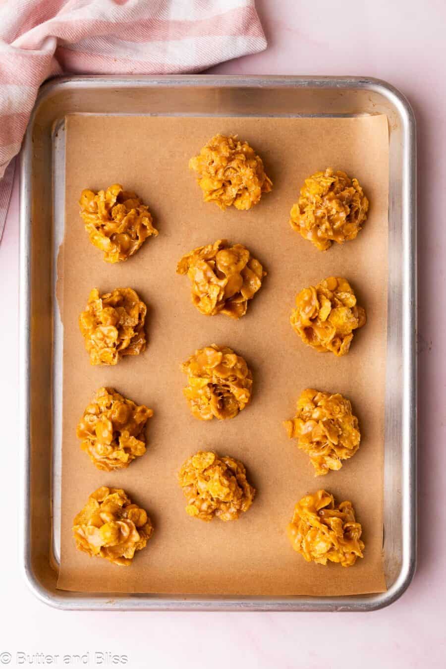 One dozen cornflake and peanut butter no-bake cookies set on a baking sheet.