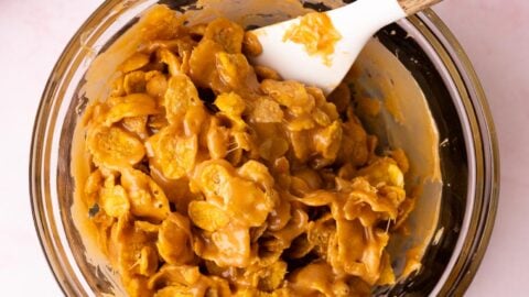 Corn flakes being mixed with peanut butter sugar syrup in a mixing bowl.
