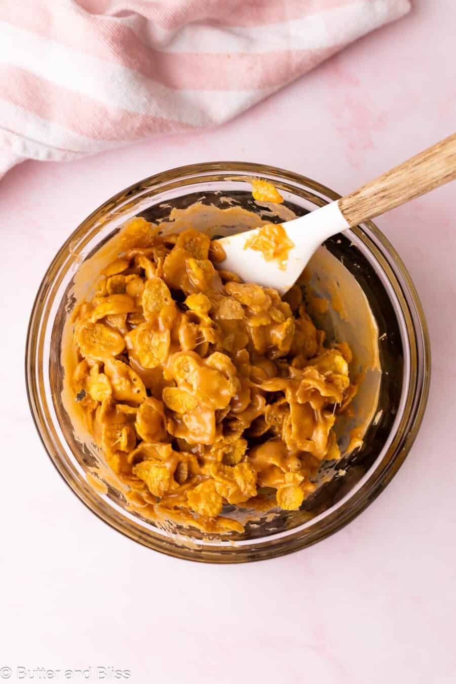 Corn flakes being mixed with peanut butter sugar syrup in a mixing bowl.