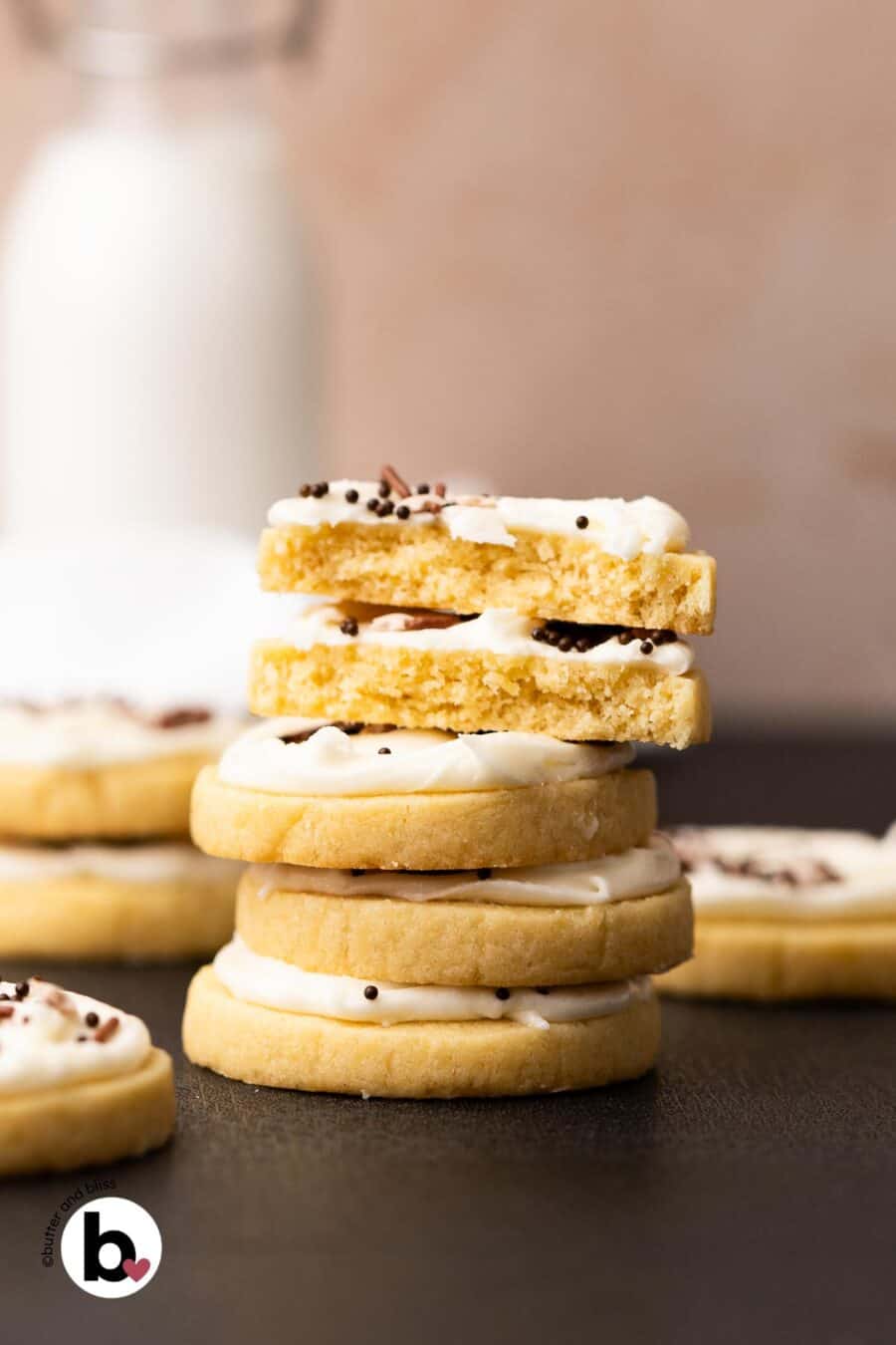 A stack of frosted butter cookies with one cut in half to reveal tender centers.