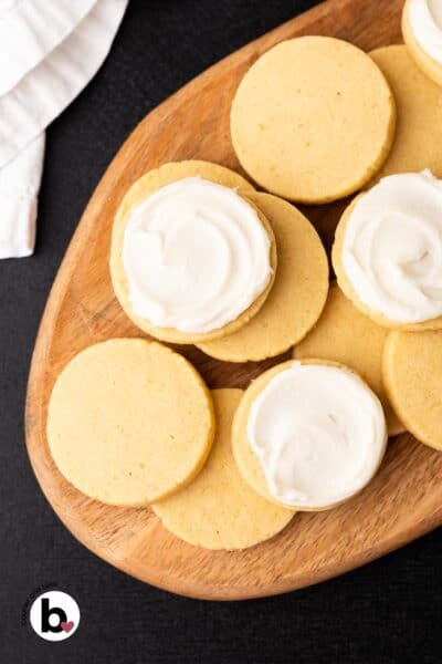 Baked butter cookies stacked on a wood plate, half of them frosted.