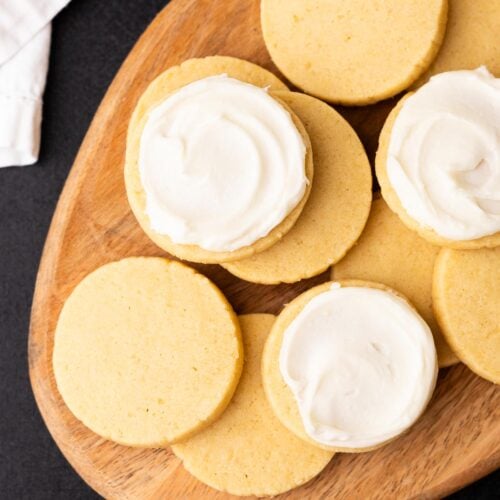 Baked butter cookies stacked on a wood plate, half of them frosted.