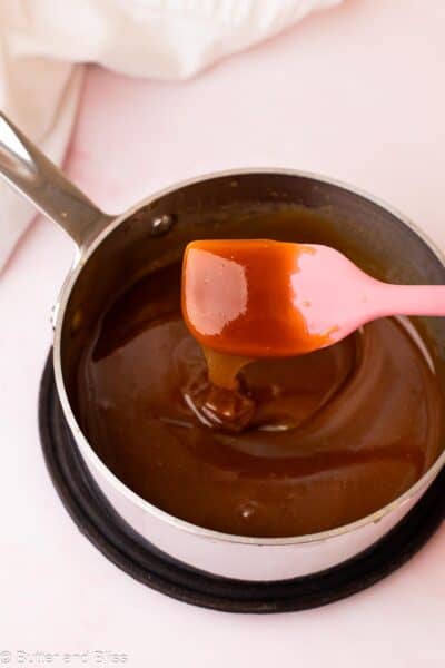 Thick and drippy maple syrup caramel sauce dripping off a pink spatula into a small saucepan.