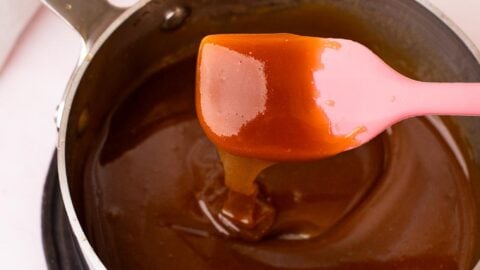 Thick and drippy maple syrup caramel sauce dripping off a pink spatula into a small saucepan.