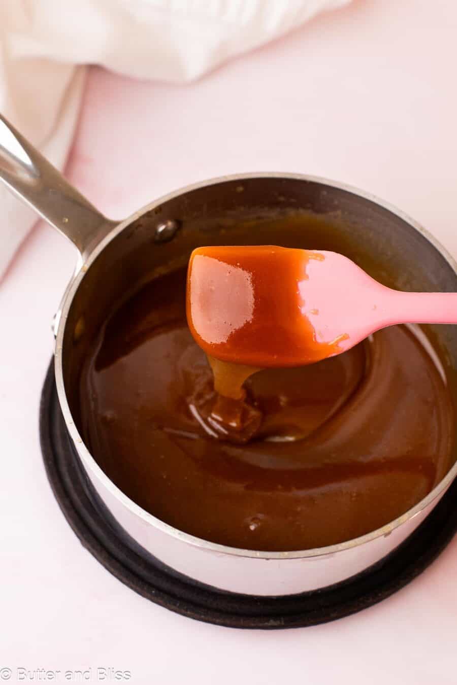 Thick and drippy maple syrup caramel sauce dripping off a pink spatula into a small saucepan.