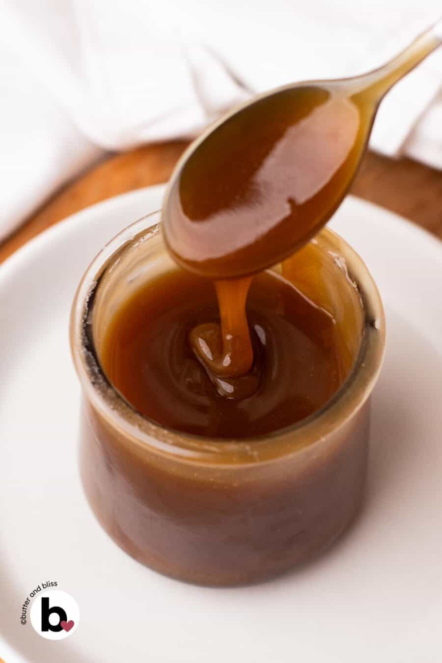 Thick maple syrup caramel sauce being dripped into a small jar with a spoon.