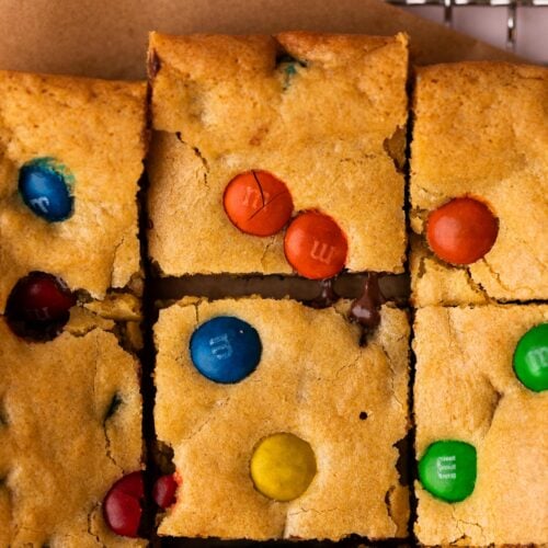 M&M cookie bars cut into square with one pulled away showing melty chocolate.