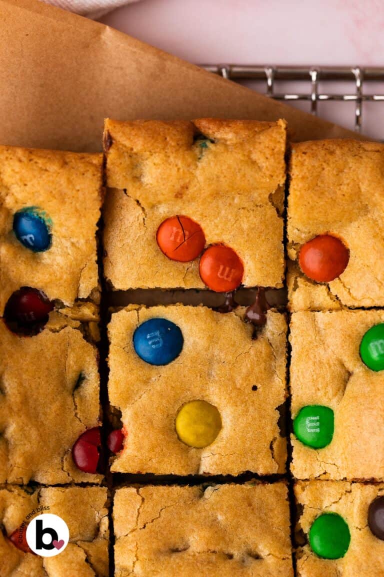 M&M cookie bars cut into square with one pulled away showing melty chocolate.