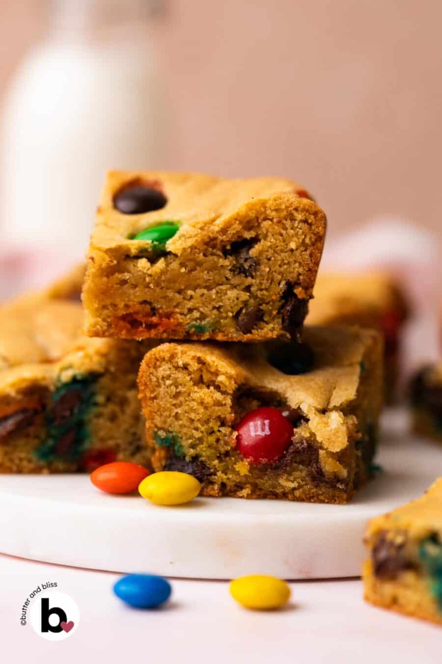 Two M&M cookie bars stacked on a white plate, surrounded by extra M&M's.