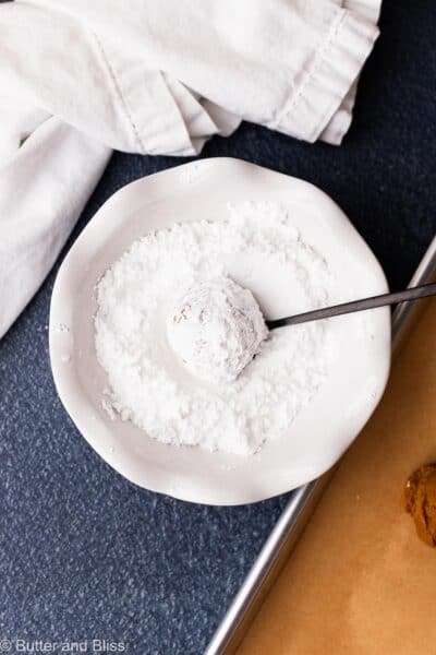 Molasses cookie rolled through powdered sugar in a white bowl.